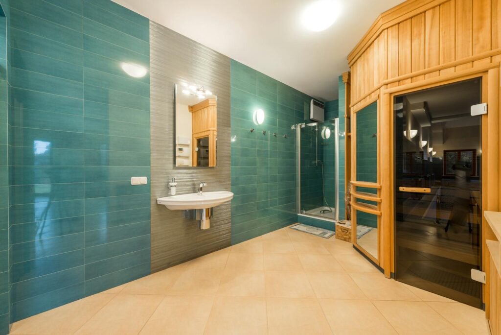 Interior of light shower room with glass cabin and sink and wooden entrance to sauna room with glass doorway