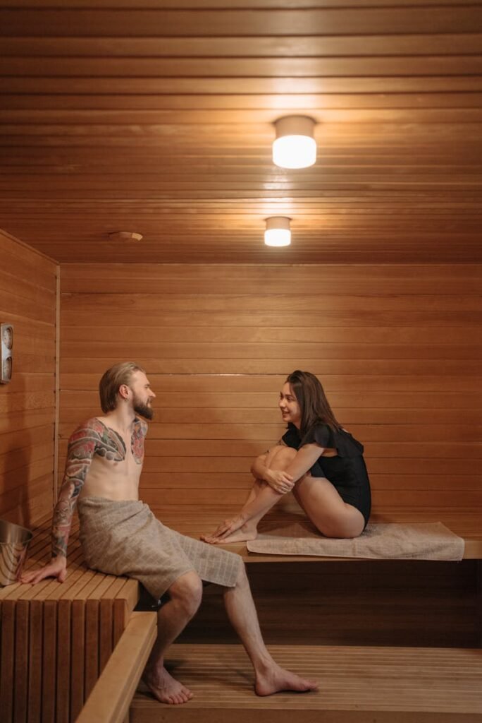 A couple relaxing and talking inside a wooden sauna room, enjoying their sauna session.