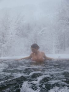 Woman enjoying a hot tub surrounded by snow-covered trees, creating a perfect winter escape.